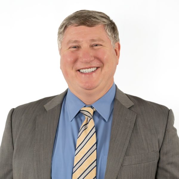 A Man Wearing A Suit And Tie Smiling At The Camera